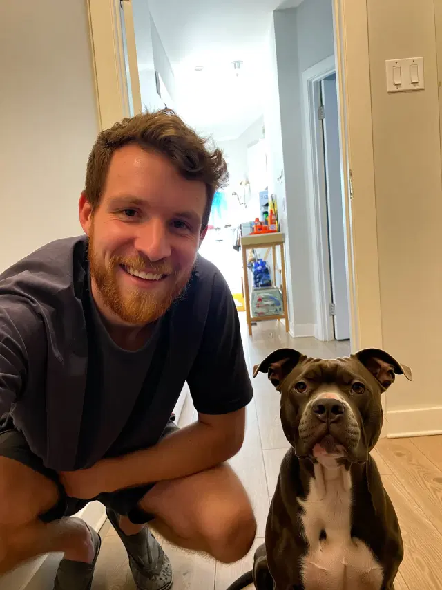 Daniel crouching next to his Pit Bull mix at home