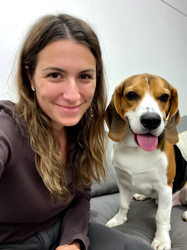 Sarah smiling on the couch beside her Beagle
